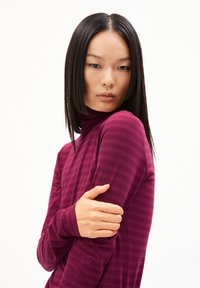 Bordeauxfarbener Rollkragenpullover mit vertikalen Streifen, der eng anliegt, lange Ärmel hat und aus weichem, glattem Material besteht. Das Modell posiert mit verschränkten Armen.