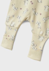 Kremasti baby outfit od mekog materijala, s ponovljenim uzorcima zečića i cvijeća, s elastičnim manžetama i obrubom.