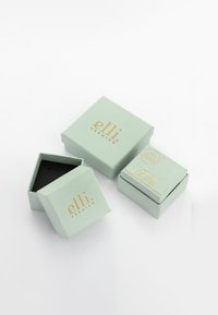 Lysgrønne rektangulære bokse med guldtekst, en åben for at afsløre et sort indre. Teksten inkluderer "elli Premium" og miljøvenlige oplysninger.