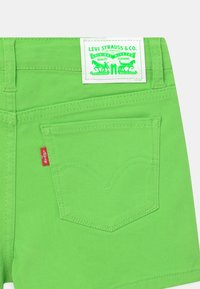 Gröna denimshorts med en bakficka som har böjd sömnad, en röd Levi's-bricka och en vit etikett med varumärket och logotypen.
