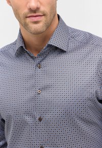 Knopen-overhemd met een geometrisch blauw en bruin patroon, kraag en bruine knopen, vervaardigd uit een lichtgewicht stof met een soepele textuur.