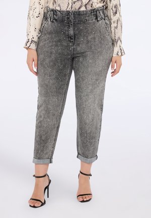 Graue Denim-Jeans mit geradem Schnitt, verziert mit kleinen silbernen Nieten und umgeschlagenen Säumen. Kombiniert mit schwarzen Sandalen mit Riemchen.