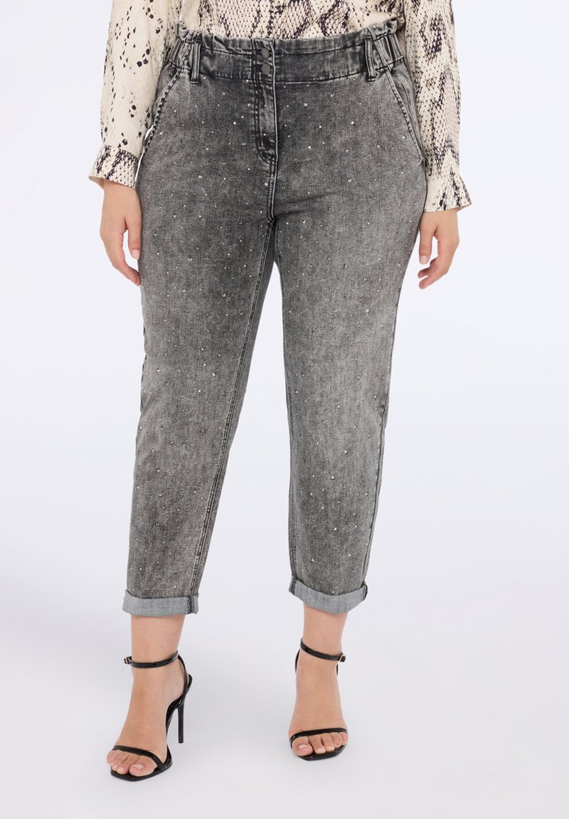 Šedé džíny z denimu se rovnými nohavicemi, zdobené malými stříbrnými cvočky a s ohrnutými lemy. V páru s černými sandály na vysokém podpatku.