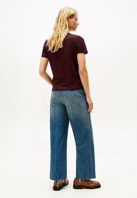 Burgunderfarbiges Baumwoll-T-Shirt kombiniert mit hellblauen, hochgeschnittenen, weit geschnittenen Jeans mit fransigen Säumen und braunen Loafers.