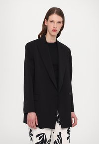 Black blazer with a tailored, oversized fit. Features a single button closure, notch lapels, and two side pockets. Worn over a black top.