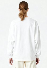 Sweat-shirt blanc à manches longues avec col rond et coupe décontractée. Le dos est uni, sans motifs, avec des épaules légèrement tombantes et des poignets.