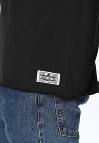 Black cotton t-shirt featuring a white label with "DENIM FACTORY." Paired with blue denim jeans showing visible stitching and a pocket.