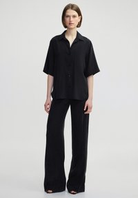 Black button-up shirt with short sleeves, made of a smooth fabric, paired with wide-leg black pants, creating a minimalist look.
