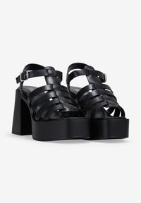Black platform sandals made of smooth leather, featuring crisscross straps, an ankle buckle, and a chunky heel.
