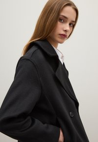 Cappotto in misto lana nero con colletto a rever, design doppiopetto e finitura testurizzata. Include bottoni e tasche.