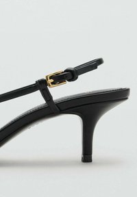 Sandal nero con tacco alto, caratterizzata da un design elegante, sottili cinturini, una fibbia in tonalità oro e una finitura liscia e lucida sul materiale in pelle.