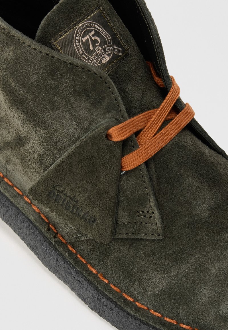 Dark green suede desert boot with orange laces, orange stitching, black sole, and a 75th anniversary label on the tongue.