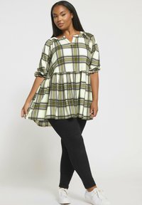 Tunika verde e bianca a quadri con scollo a V e maniche a sbuffo, abbinata a pantaloni neri aderenti e sneakers bianche. Tessuto misto cotone.
