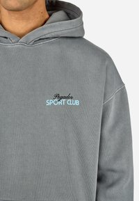 Sivá mikina s kapucňou s jemnou textúrou. Čierny a svetlomodrý nápis "Pegador SPORT CLUB." Uvoľnený strih s klasickým dizajnom.