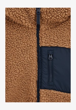 Brun fluffig fleece-tyg med en strukturerad yta, kontrasterande svart nylonpanel och dragkedjedetaljer. Har en hel dragkedjestängning fram.