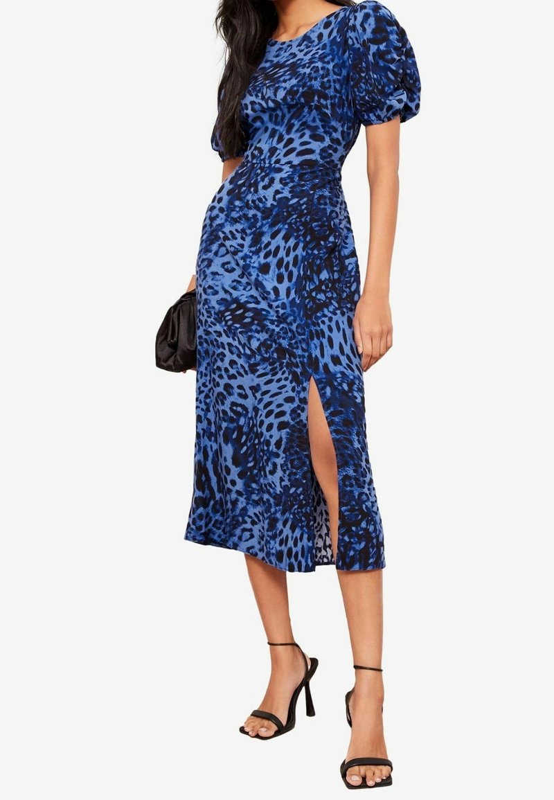 Robe à imprimé animal bleu avec des manches bouffantes, fente jusqu'au genou, texture lisse, design ajusté, associée à des talons aiguilles noirs et une pochette.