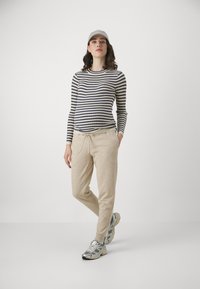Stripete langermet topp i marineblå og krem, paret med beige joggebukser. Tilbehør inkluderer en lysekrone cap og joggesko med sølvdetaljer.