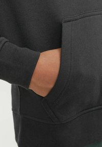 Felpa nera con una texture morbida. Dotata di tasca a marsupio e polsini a costine. Design semplice senza motivi o decorazioni.