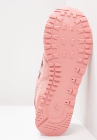 Semelle de chaussure rose avec des motifs de crampons profonds et épais conçus pour l'adhérence et la durabilité, photographiée sur un fond blanc.