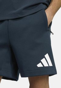 Marineblauwe sportshorts van textuurstof, met een schuin wit drie-strepen logo, zijzakken en een trekkoord-detail.