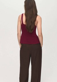 Burgundin fitted tank top, jossa on peplum-helma, yhdistetty ruskeisiin leveälahkeisiin housuihin. Pehmeä kangas, jossa on hieno kiilto. Näyttää takaa.