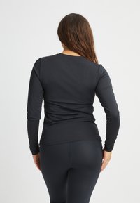 Musta pitkähihaine paita pyöreällä pääntiellä ja sileällä pinnalla, yhdistettynä tummiin leggingsseihin. Venytettävä, käyttömukavuutta tarjoava muotoilu.