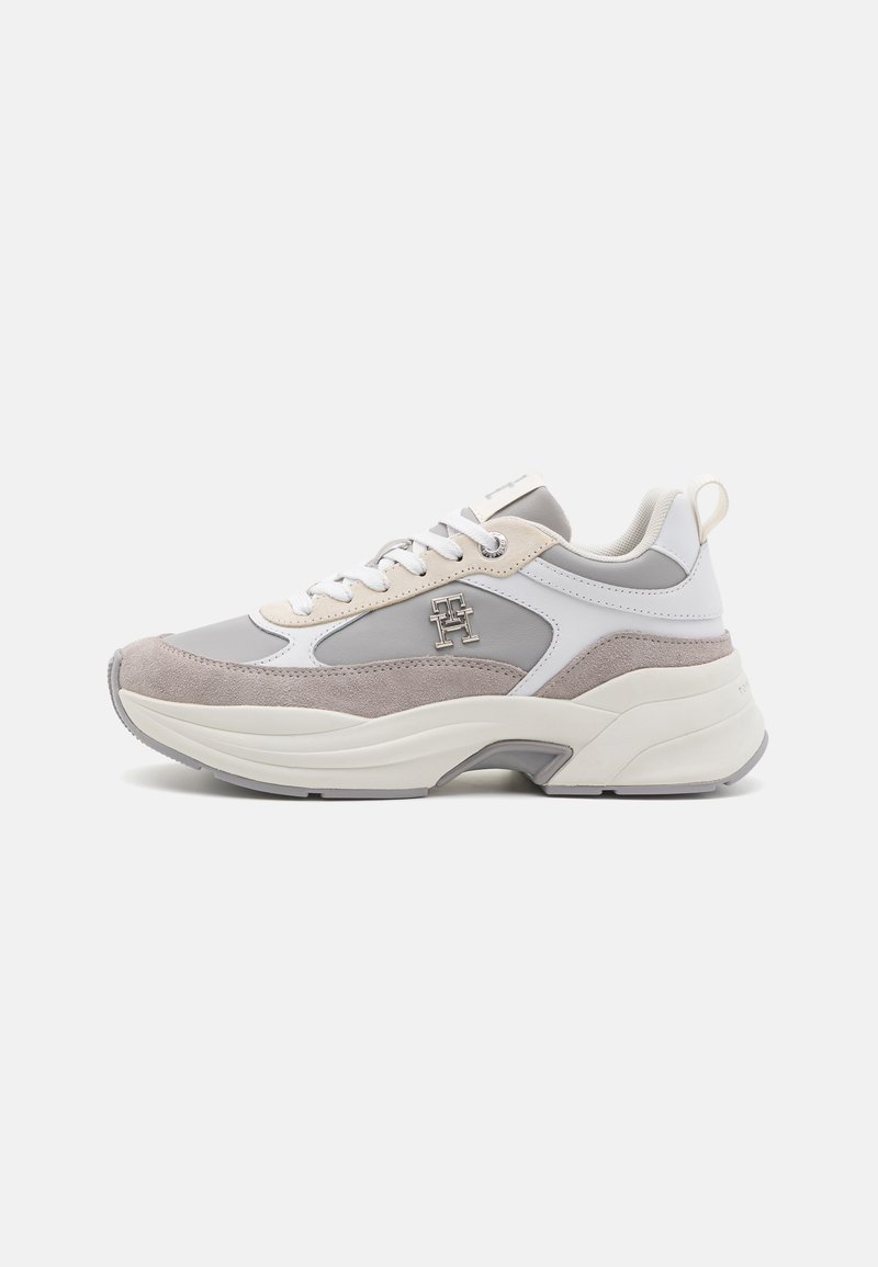Zapatillas que combinan cuero gris y blanco con un superpuesto de ante texturizado, suela gruesa y un acento metálico del logo en el costado.