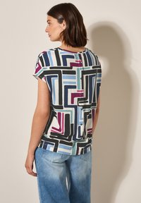 Chemise à manches courtes en tissu léger, arborant un motif géométrique en noir, bleu, violet et bleu-vert, avec des boutons dans le dos.