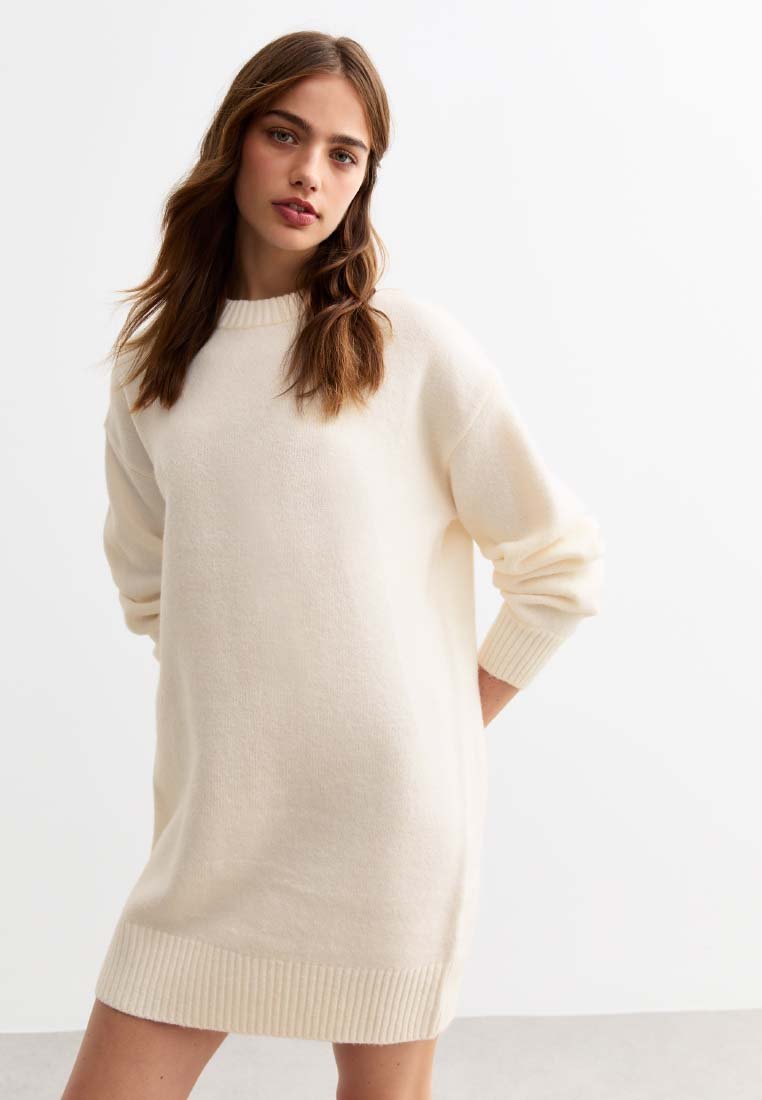 Crème-kleurige gebreide trui-jurk met geribbelde ronde hals en mouwen. Heeft lange mouwen en een rechte, relaxte pasvorm op midi-dij lengte.