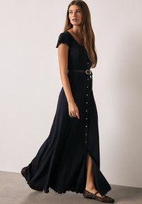 Fekete maxi ruha gombos elülső résszel, rövid fodros ujjal és fekete, deréknál szűkített övvel. Oldalsó hasítékkal és folyékony szegéllyel rendelkezik.