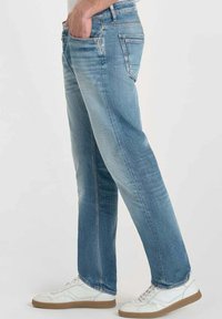 Jeans de mezclilla azul claro con un acabado ligeramente desgastado, diseño de pierna recta y bolsillos frontales. Llevado con zapatillas blancas.
