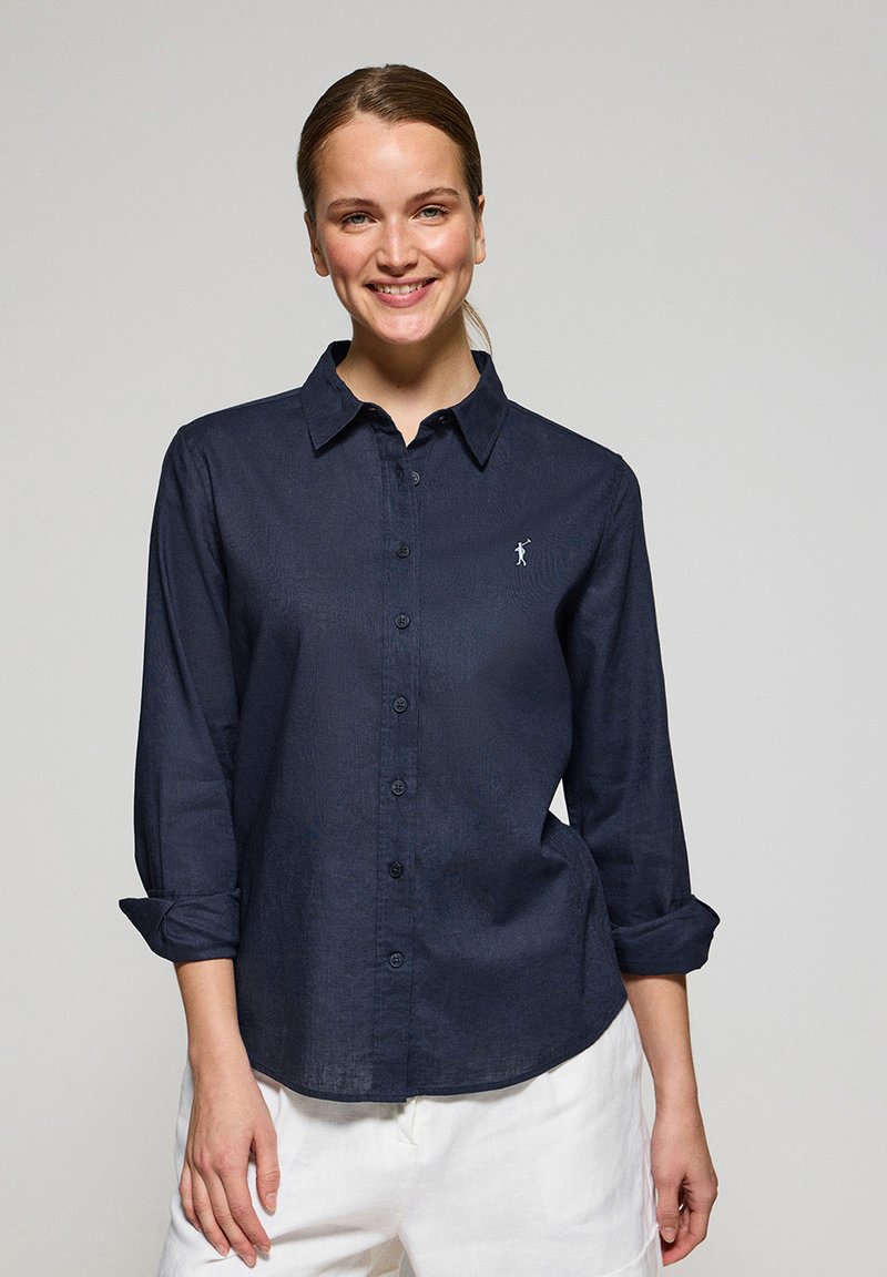 Navy button-up shirt made of linen, featuring long sleeves with rolled cuffs and a small embroidered logo on the left chest.