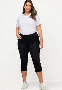 Vaqueros negros cortos de corte ajustado, con bolsillos delanteros y una textura suave, combinados con una camiseta blanca básica y zapatillas blancas.