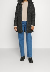 Padded black parka with a quilted pattern, front zipper, and a hood, worn over a beige sweater and blue straight-leg jeans. Black ankle boots.