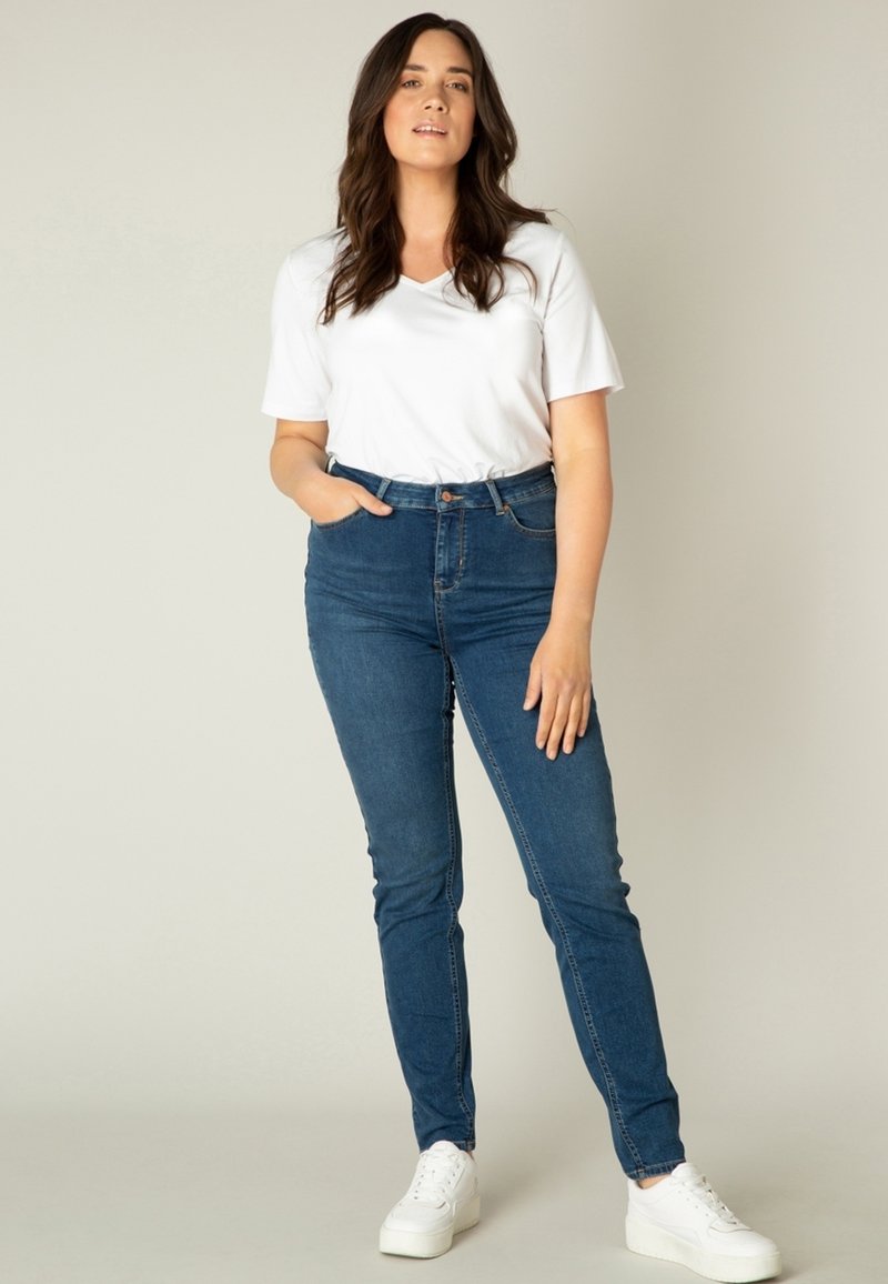 Blauwe skinny jeans met een hoge taille, gedragen met een witte V-hals t-shirt en witte sneakers. Glad denim textuur, minimalistisch ontwerp.