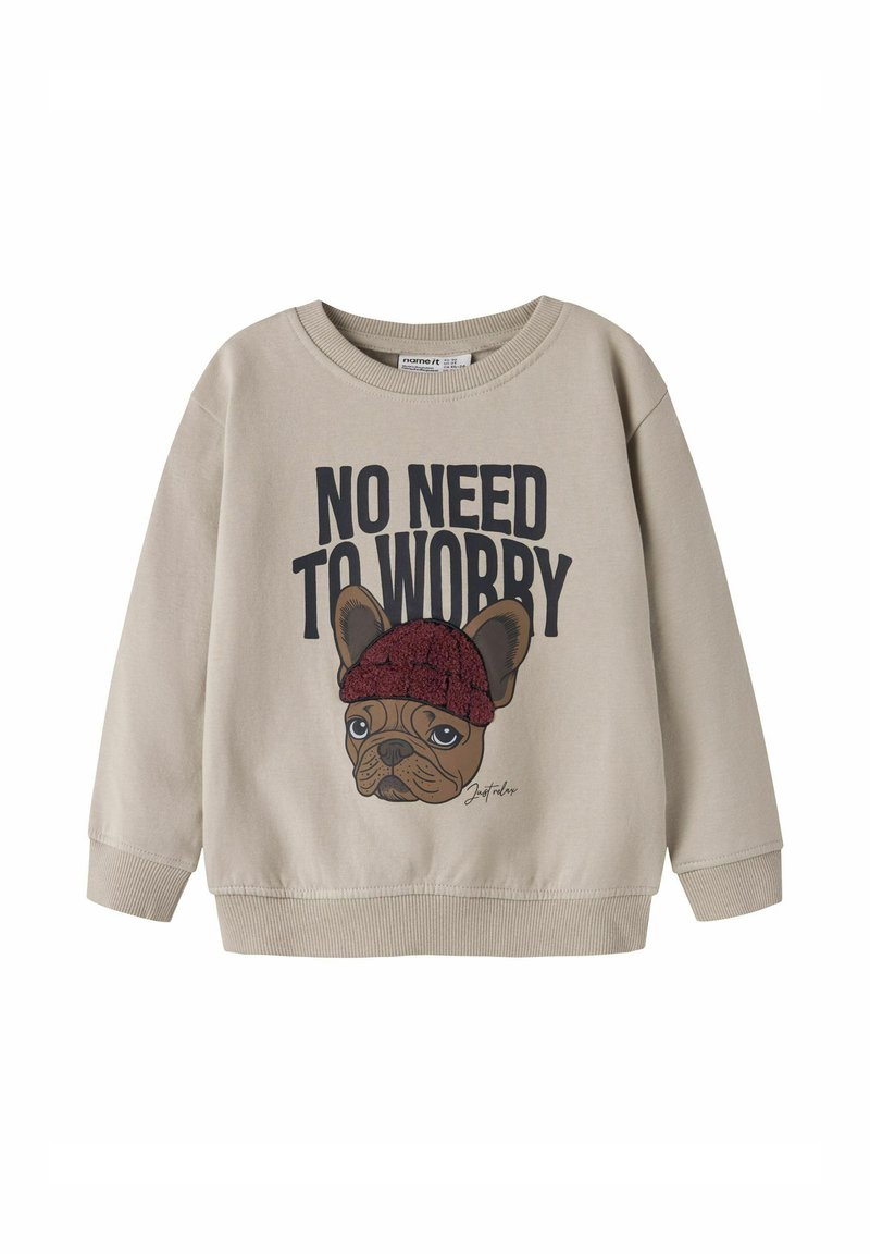 Sweat-shirt beige présentant un bulldog français en dessin animé portant un bonnet rouge, avec le texte "PAS BESOIN DE S'INQUIÉTER" au-dessus.