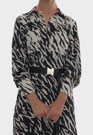 Czarna i kremowa sukienka na guziki w zebrę z dwoma kieszeniami na piersi, długimi rękawami oraz szerokim czarnym paskiem z złotym akcentem.