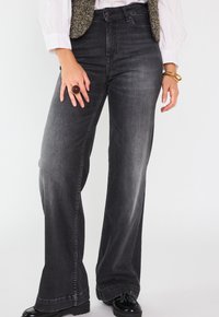 Jean noir taille haute évasé en denim avec un aspect décoloré. Comprend des poches avant et arrière, des coutures élégantes et une large ouverture de jambe.