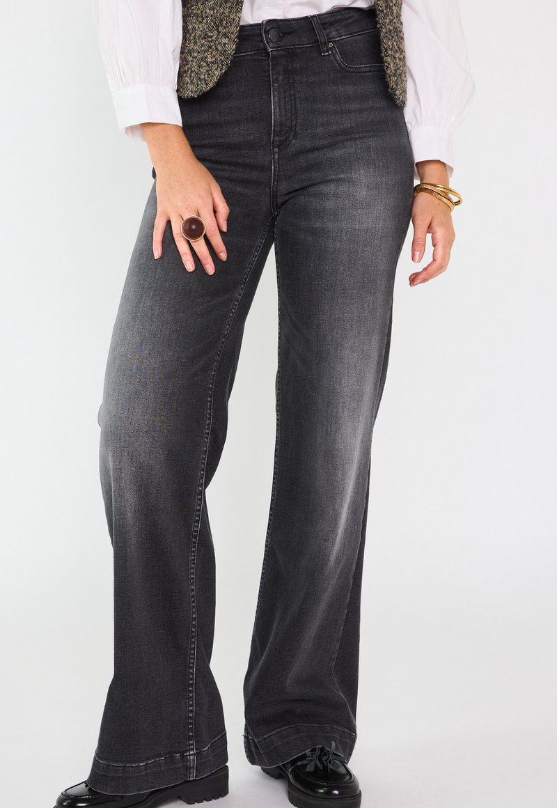 Jean noir taille haute évasé en denim avec un aspect décoloré. Comprend des poches avant et arrière, des coutures élégantes et une large ouverture de jambe.