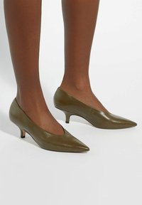 Olive green leather pointed-toe heels with a low kitten heel and a cut-out detail on the sides, smooth texture and clean design.