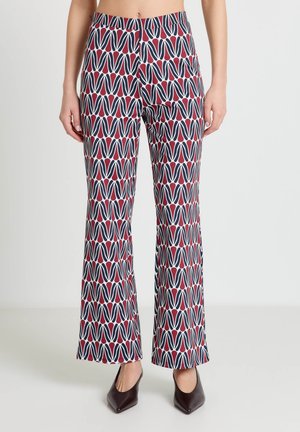 Pantaloni con motivo geometrico in blu navy e rosso, indossati con décolleté scure con punta appuntita, mostrati dalla vita ai piedi.