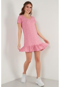 Roze jurk met korte mouwen, een V-hals, een witte bloemenpatroon en een geribbelde zoom. Gekleed met witte sneakers. Glad, lichtgewicht stof.