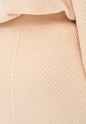 Light beige knit fabric with a textured, ribbed pattern, featuring diagonal lines and a soft, stretchy appearance. Close-up view.