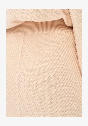 Lichtbeige gebreide stof met een gestructureerd, geribbeld patroon, met diagonale lijnen en een zachte, rekbare uitstraling. Close-up weergave.