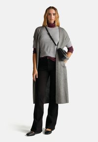 Długi szary kardigan na jasnoszarym swetrze i burgundowym golfie w paski, połączony z czarnymi spódnicami dzwonami i czarnymi balerinami.