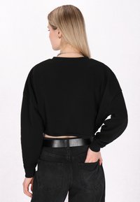 Felpa nera corta con maniche lunghe, polsini a costine e scollatura rotonda, abbinata a jeans neri a vita alta e una cintura lucida.