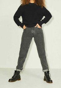 Maglione nero a coste, jeans grigi a vita alta e stivali neri con lacci e suola spessa. Vestibilità rilassata con polsini arrotolati sui jeans.