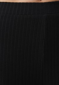 Tissu noir côtelé avec des lignes verticales. Le matériau est extensible, doté d'une large ceinture et d'une texture lisse, idéal pour les vêtements de sport.