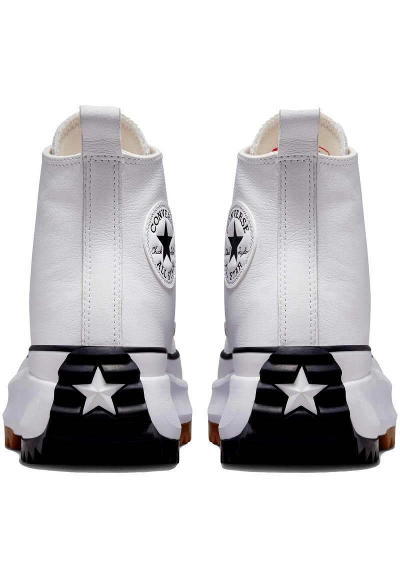 Baskets montantes blanches en cuir avec une semelle en caoutchouc noire et blanche, arborant un logo étoile noir distinctif et des détails de couture blanche.
