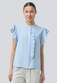 Light blue short-sleeve blouse with a ruffled front, button closure, and mandarin collar. Smooth texture, falls slightly below the waist.